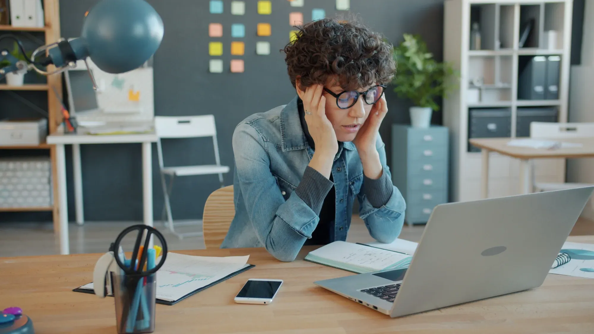 Person sitting at a desk with hands on their temples, looking stressed while staring at a laptop