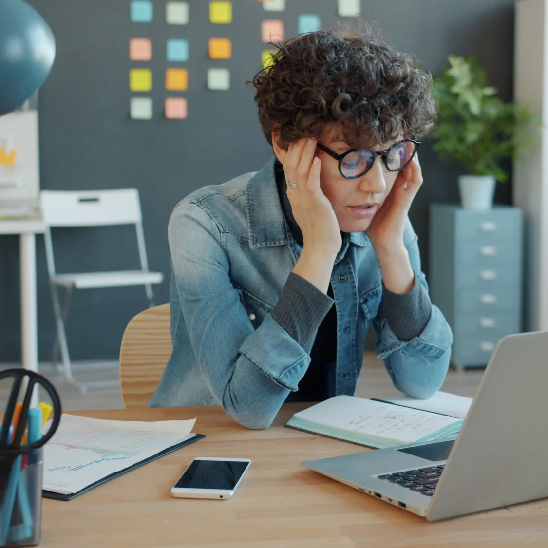 Person sitting at a desk with hands on their temples, looking stressed while staring at a laptop